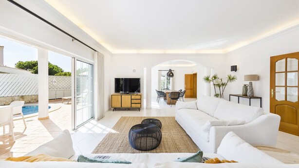 A spacious living room with a white sofa, a TV, and a dining area with a table and chairs. - Casa Flores - Five Bedroom Villa, Sleeps 10 (Vale Garrão)