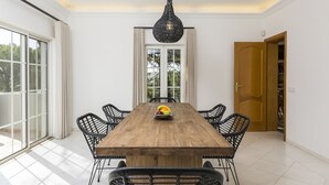 A dining area with a wooden table, black chairs, a fruit bowl, and a hanging light fixture. - Casa Flores - Five Bedroom Villa, Sleeps 10 (Vale Garrão)