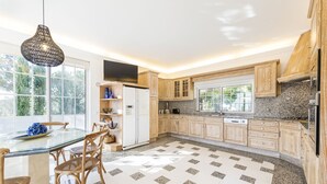 A modern kitchen with wooden cabinets, a granite countertop, and a glass dining table with wicker chairs. - Casa Flores - Five Bedroom Villa, Sleeps 10 (Vale Garrão)