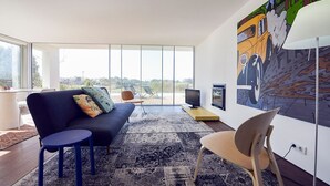 A modern living room with a sofa, a small table, a chair, a TV, and a large window offering a view of the outdoors. - Caminha Views - Two Bedroom Villa, Sleeps 4 (Moledo)