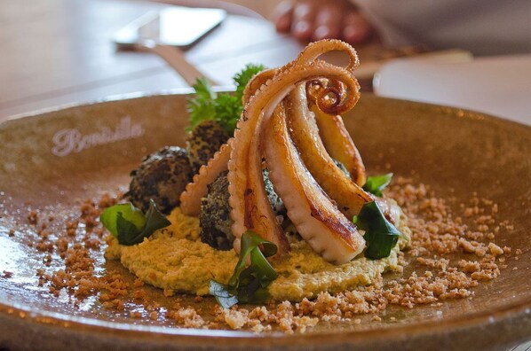 A dish with octopus, greens, and crumbled elements on a plate.