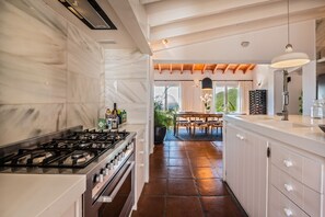 A modern kitchen with a gas stove, white cabinetry, and a dining area with a table and chairs.