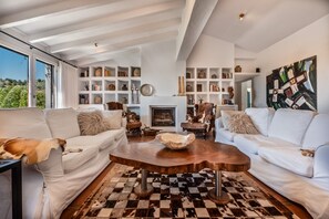 A spacious living room with a fireplace, white sofas, a coffee table, and a large abstract painting.