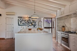 A modern kitchen with a central island, pendant lighting, and a large abstract painting on the wall. - Blanco De Caza - Three Bedroom Villa, Sleeps 6 (Alcaucín)