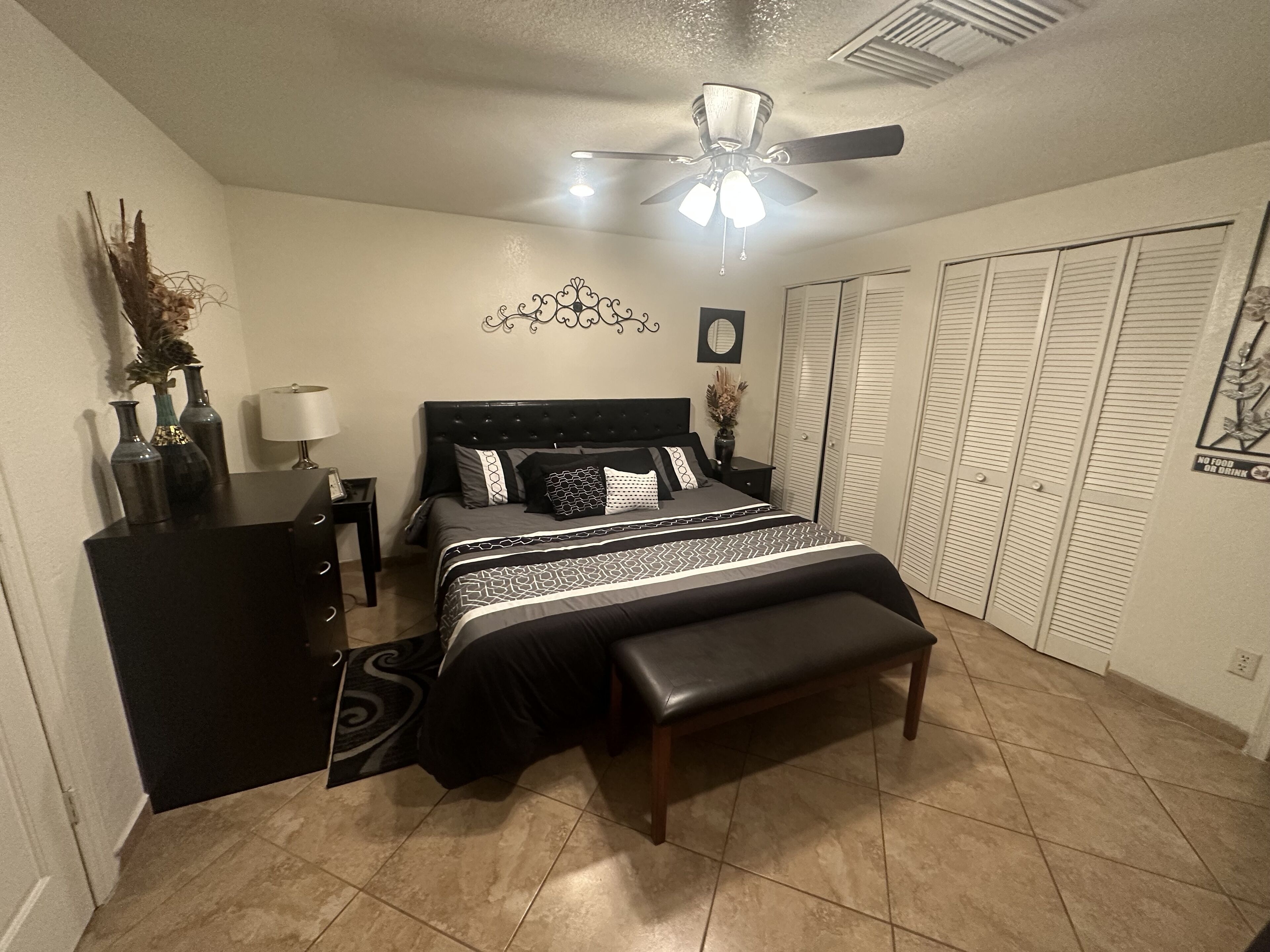 A bedroom with a bed, a desk, a chair, a ceiling fan, and a wardrobe.
