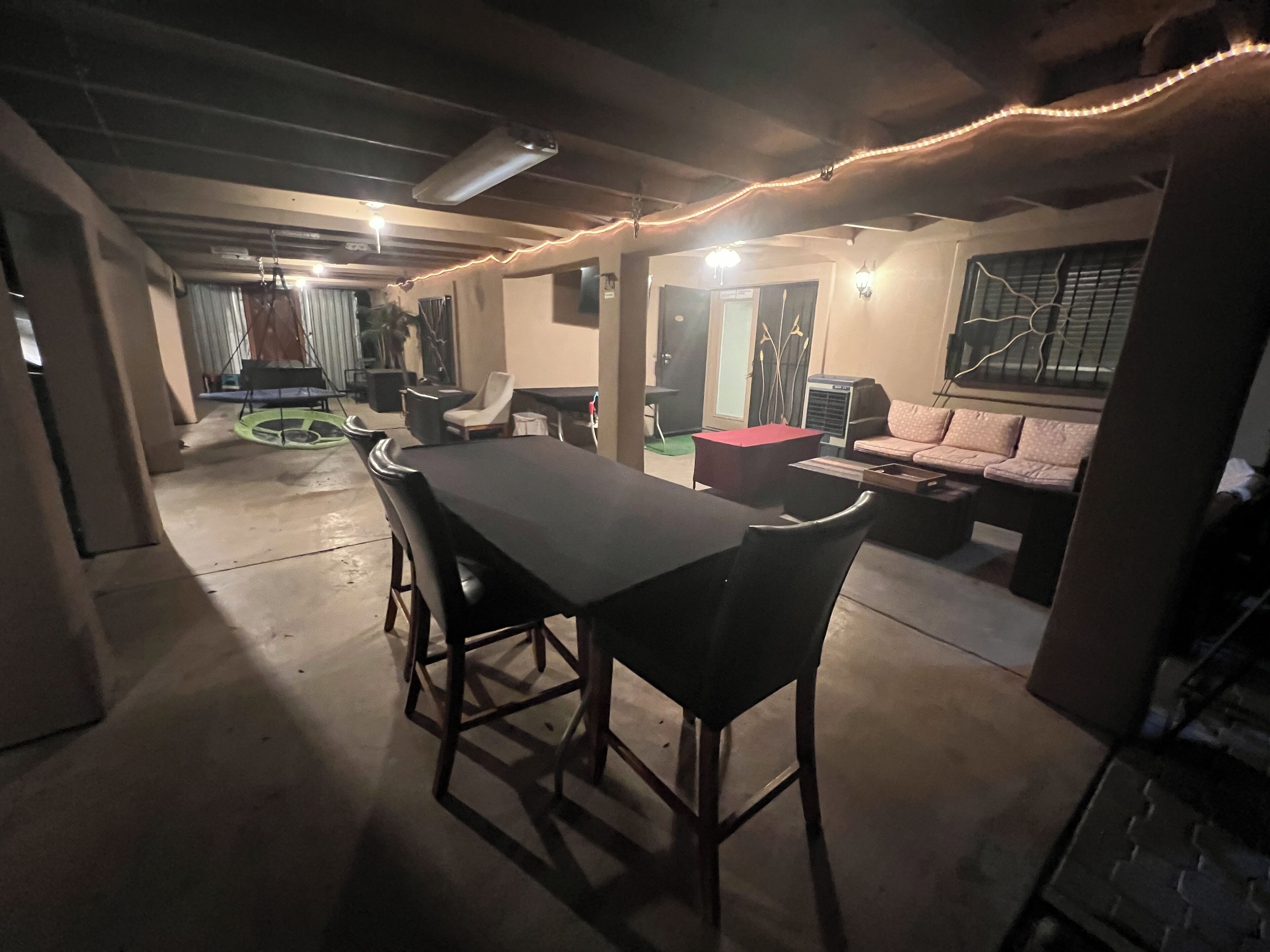 A spacious room with a long table and chairs, a sofa, and a small red ottoman.
