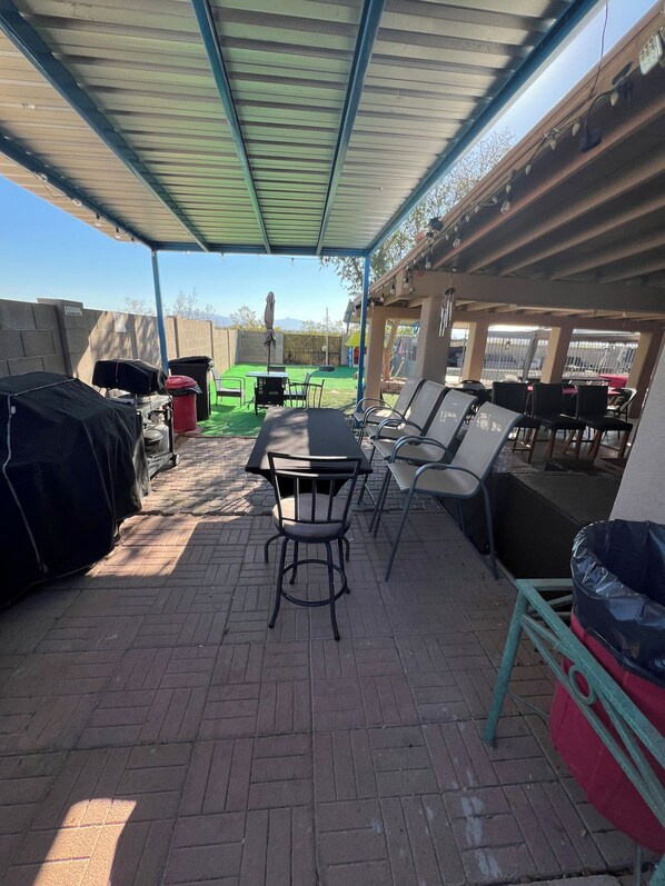 An outdoor patio area with a covered seating area, a grill, and a table with chairs.