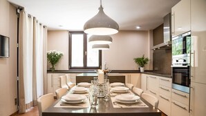 A modern kitchen with a central island, built-in appliances, and a dining area set up for a meal. - Can Marta - Four Bedroom Apartment, Sleeps 8 (Deya)