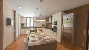 A modern kitchen with a central island, stainless steel appliances, and a dining area set for six. - Can Marta - Four Bedroom Apartment, Sleeps 8 (Deya)
