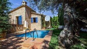 Una casa de piedra con piscina, antena parabólica y un gran árbol.