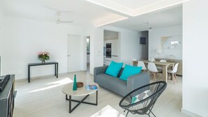 Ein modernes Wohnzimmer mit einem grauen Sofa, einem schwarzen Sessel und einem Couchtisch. Im Hintergrund befindet sich ein Essbereich mit Tisch und Stühlen.