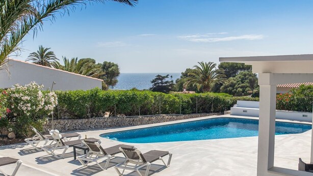 Ein Swimmingpool mit Liegestühlen, einer Steinmauer und Blick auf das Meer.