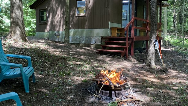 Une cabane avec un foyer, une terrasse en bois et deux chaises bleues.