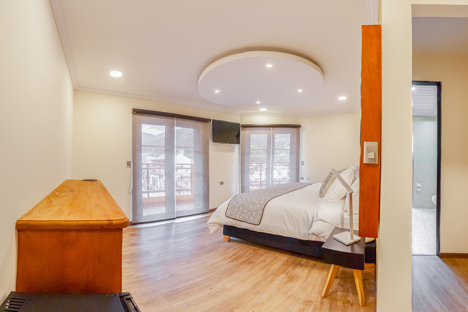 A modern bedroom with a bed, a wooden nightstand, and a sliding glass door leading to an outdoor area.