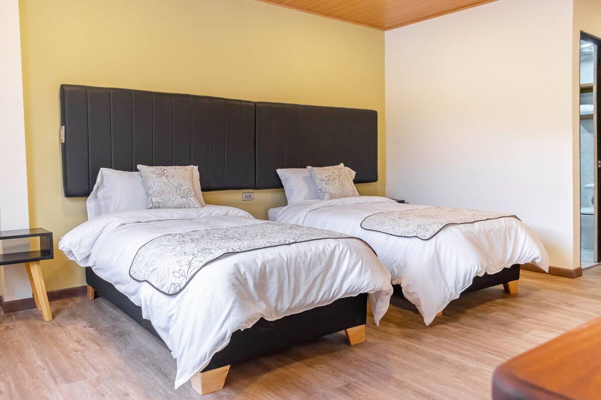 Una cama doble con cabecera oscura, dos mesitas de noche y suelo de madera.