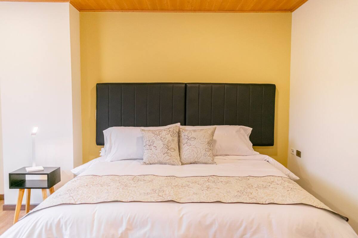 Una cama bien hecha con un cabecero oscuro, sábanas blancas y almohadas con estampado floral.