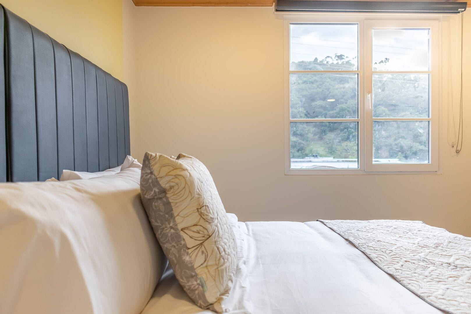 Ein Schlafzimmer mit Bett, Fenster mit Blick auf Grünflächen und einem Kopfteil.