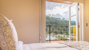 Un dormitorio con cama, vista a un balcón con barandilla y puerta de acceso al exterior.