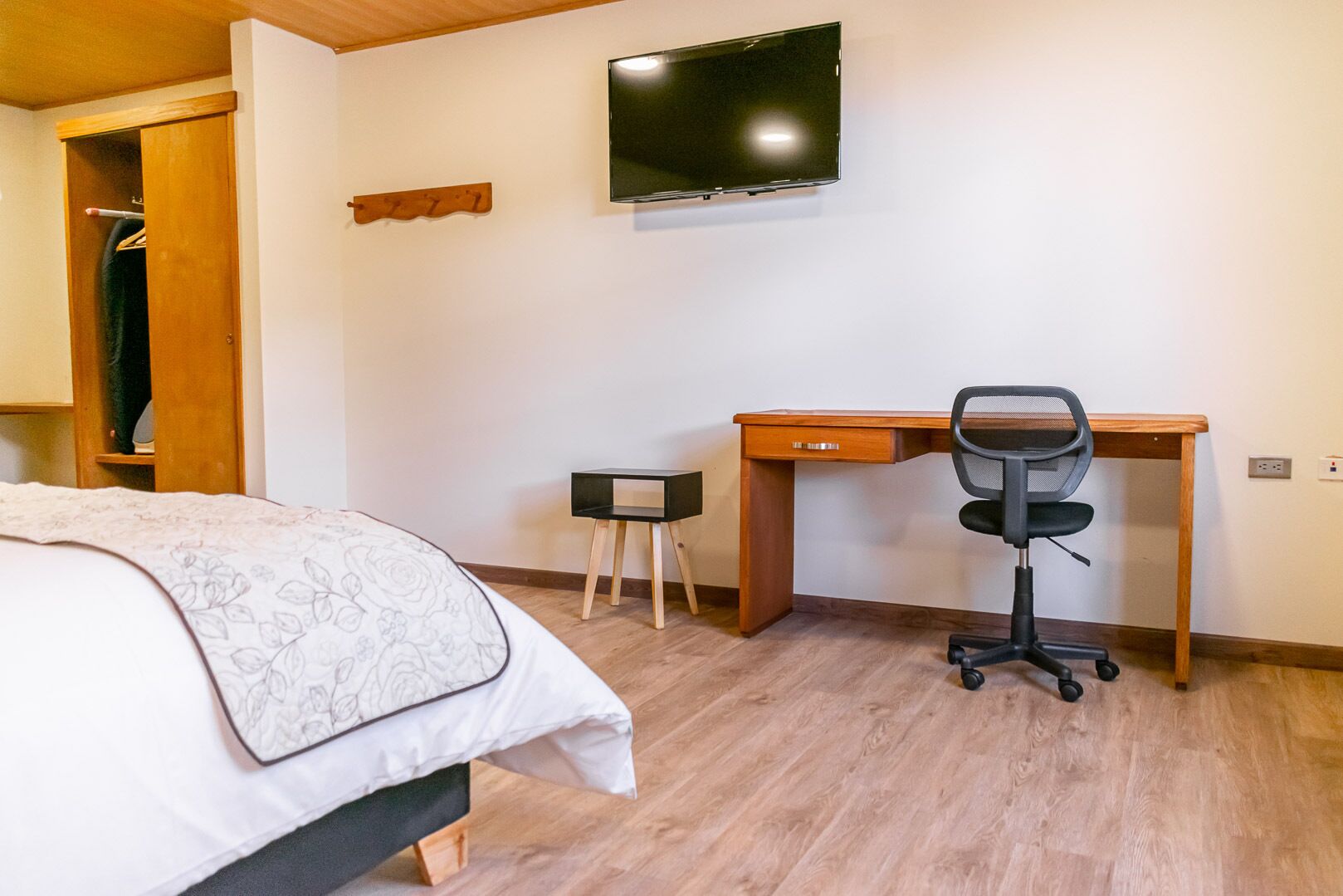 A bedroom with a bed, a desk, a chair, a TV, and a wooden wardrobe.
