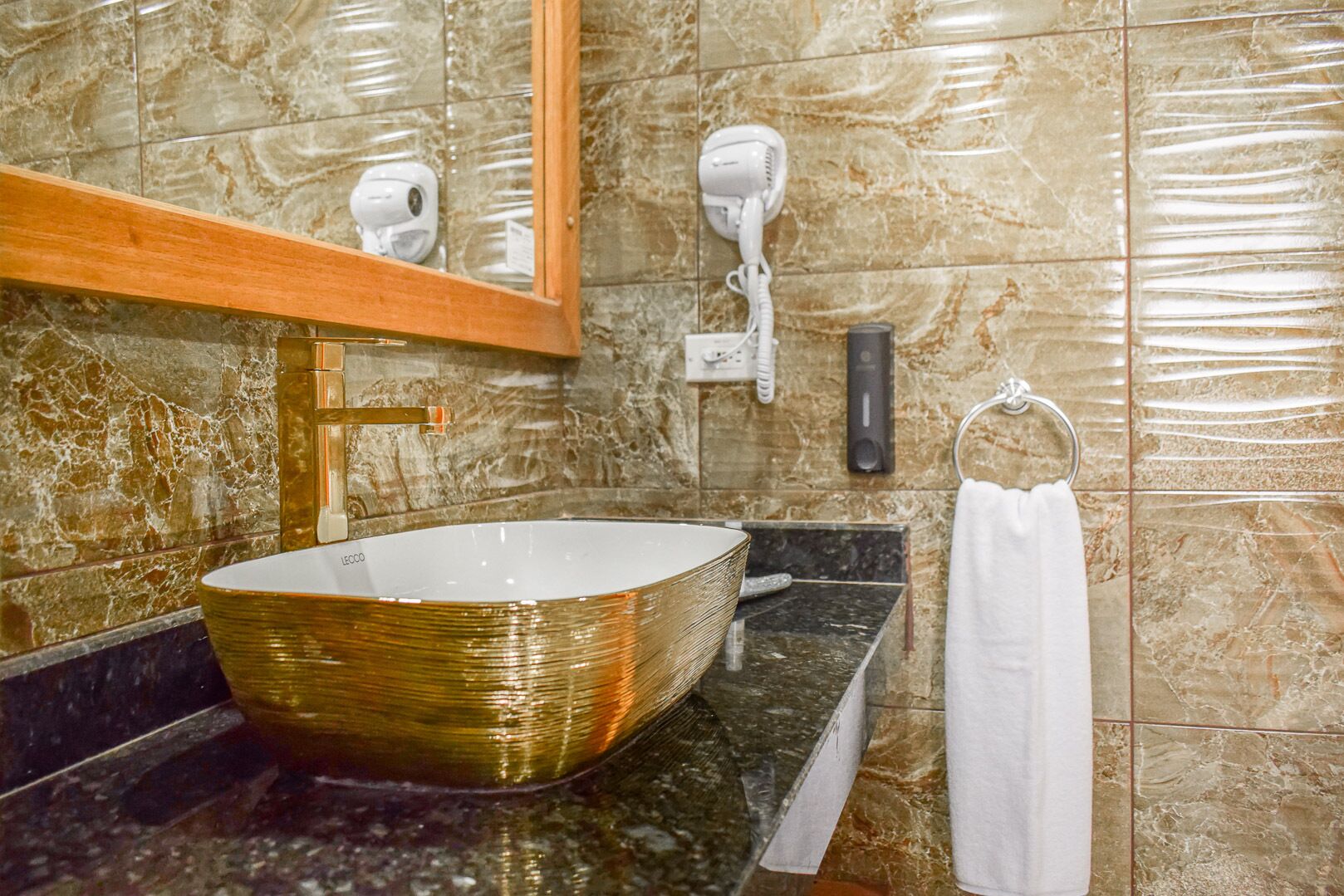 A bathroom with a large, oval-shaped vessel sink, a wooden-framed mirror, and a towel rack with a white towel.