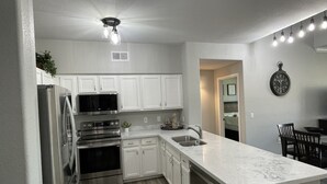 A modern kitchen with white cabinets, stainless steel appliances, a marble countertop, and a built-in oven.