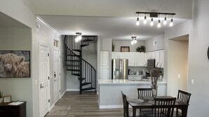 A modern kitchen with a central island, white cabinetry, and a black staircase.