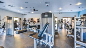 A gym with various exercise machines, a ceiling fan, and a large mirror.