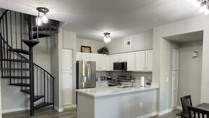 A modern kitchen with a central island, stainless steel appliances, and a black spiral staircase.