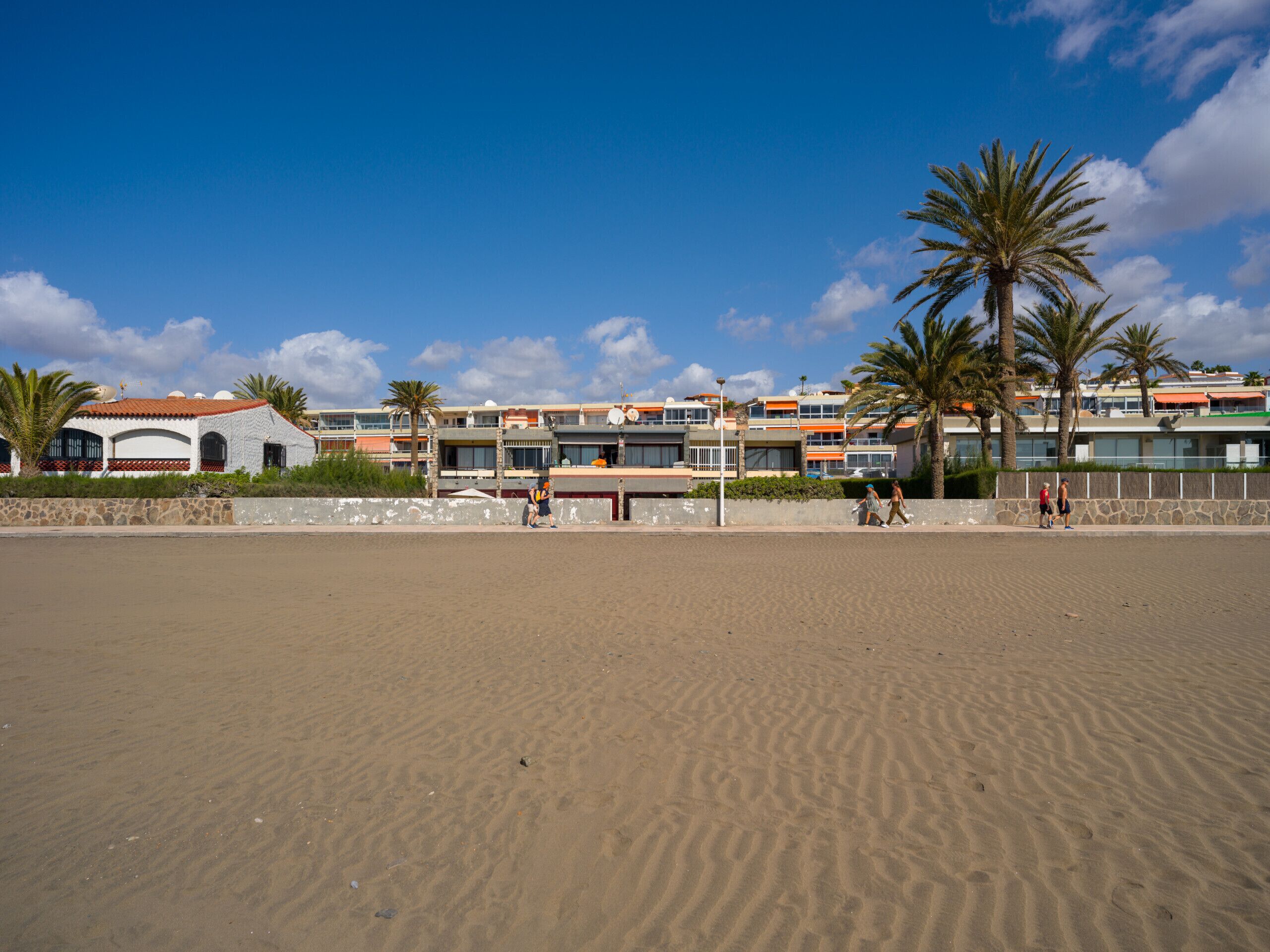 Ett hotell vid stranden med flera byggnader, palmer och en sandstrand.