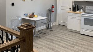 A modern kitchen with white cabinets, a microwave, and a stove. There is a dining table with chairs and a decorative wall art piece. - Ambiance by the Falls Cozy Suite (Niagara Falls)