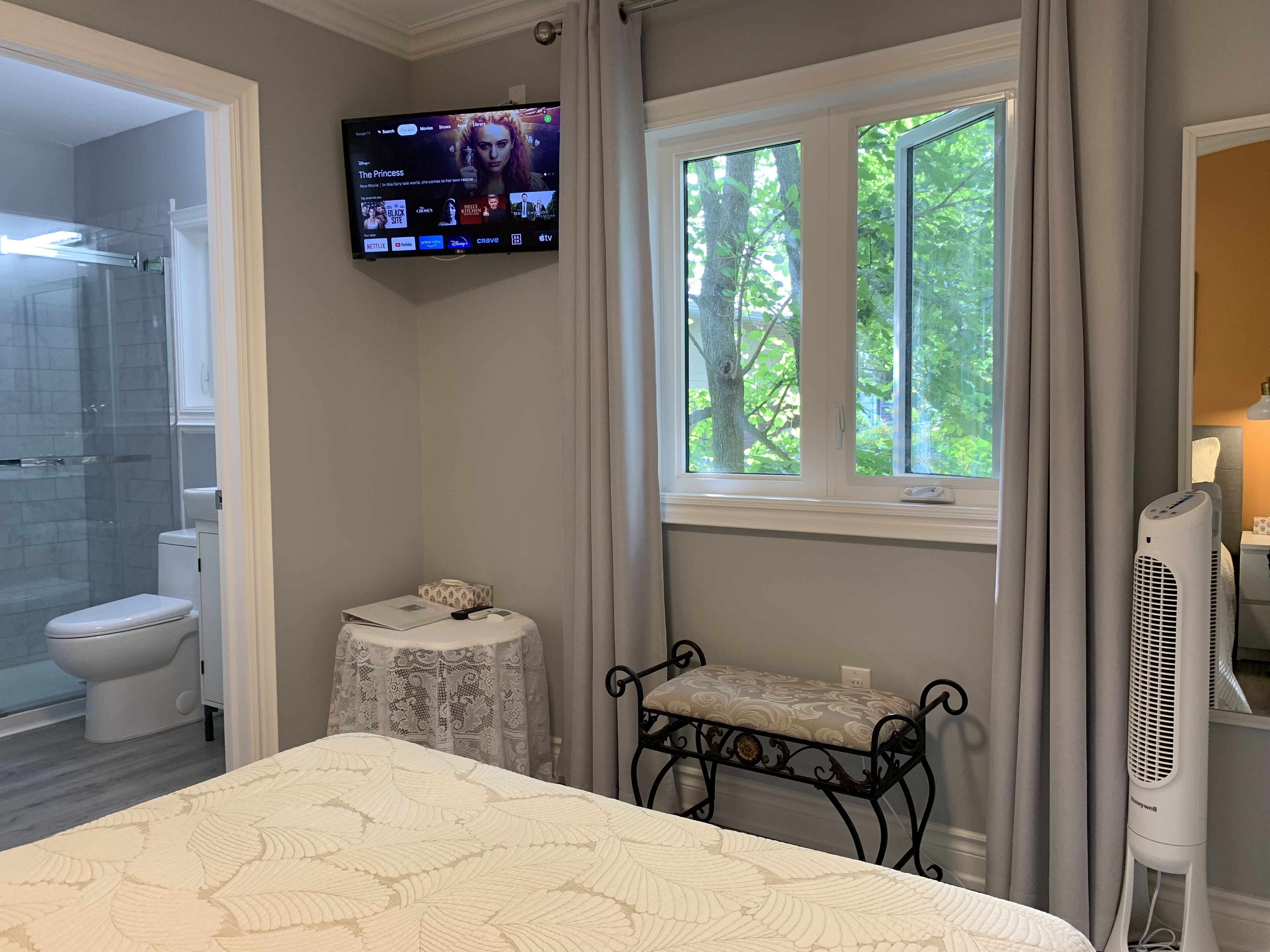 Un baño con ducha, inodoro y televisor de pared que muestra una película.