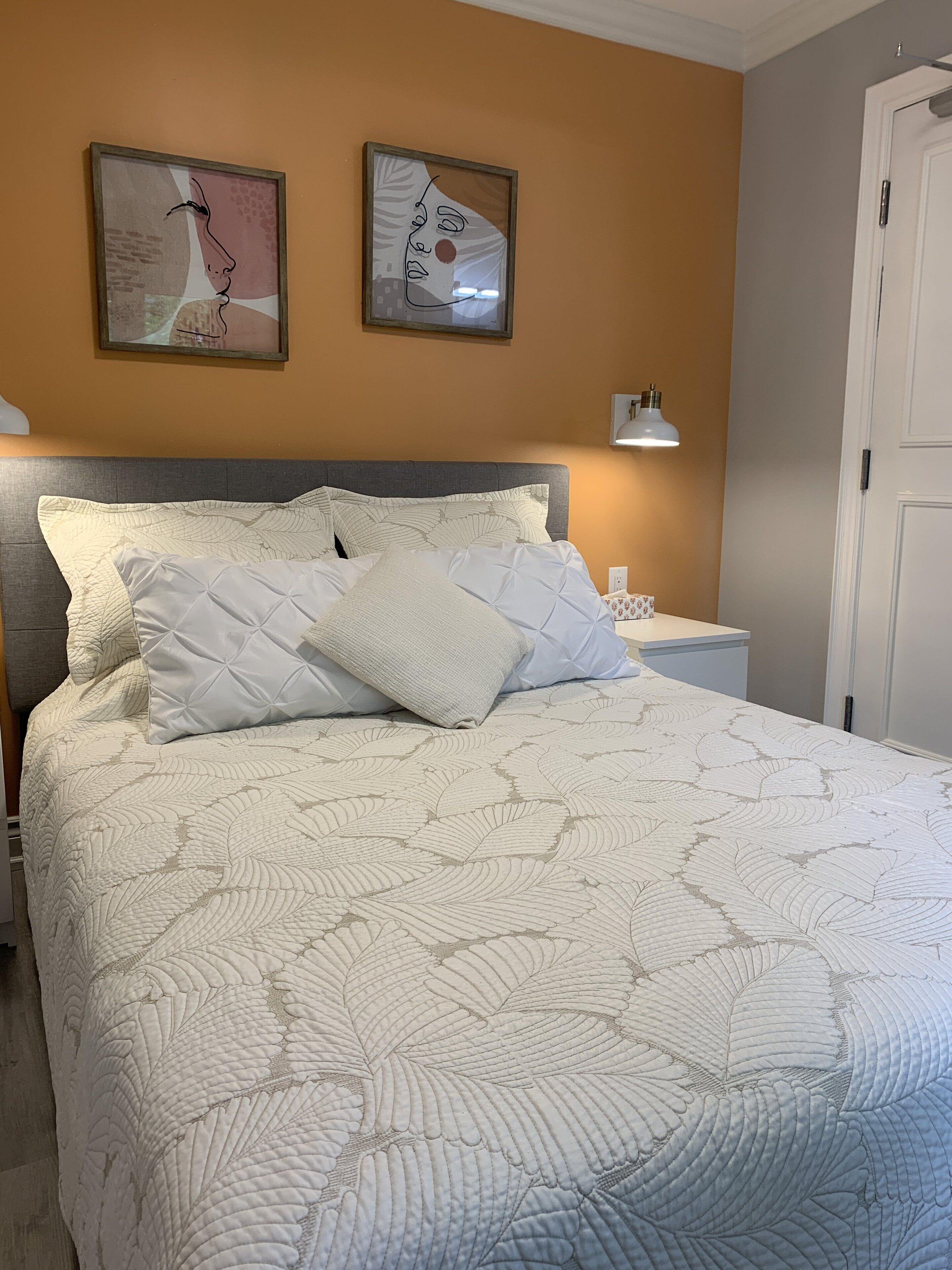 A neatly made bed with a patterned quilt, a bedside table with a lamp, and two framed artworks on the wall.