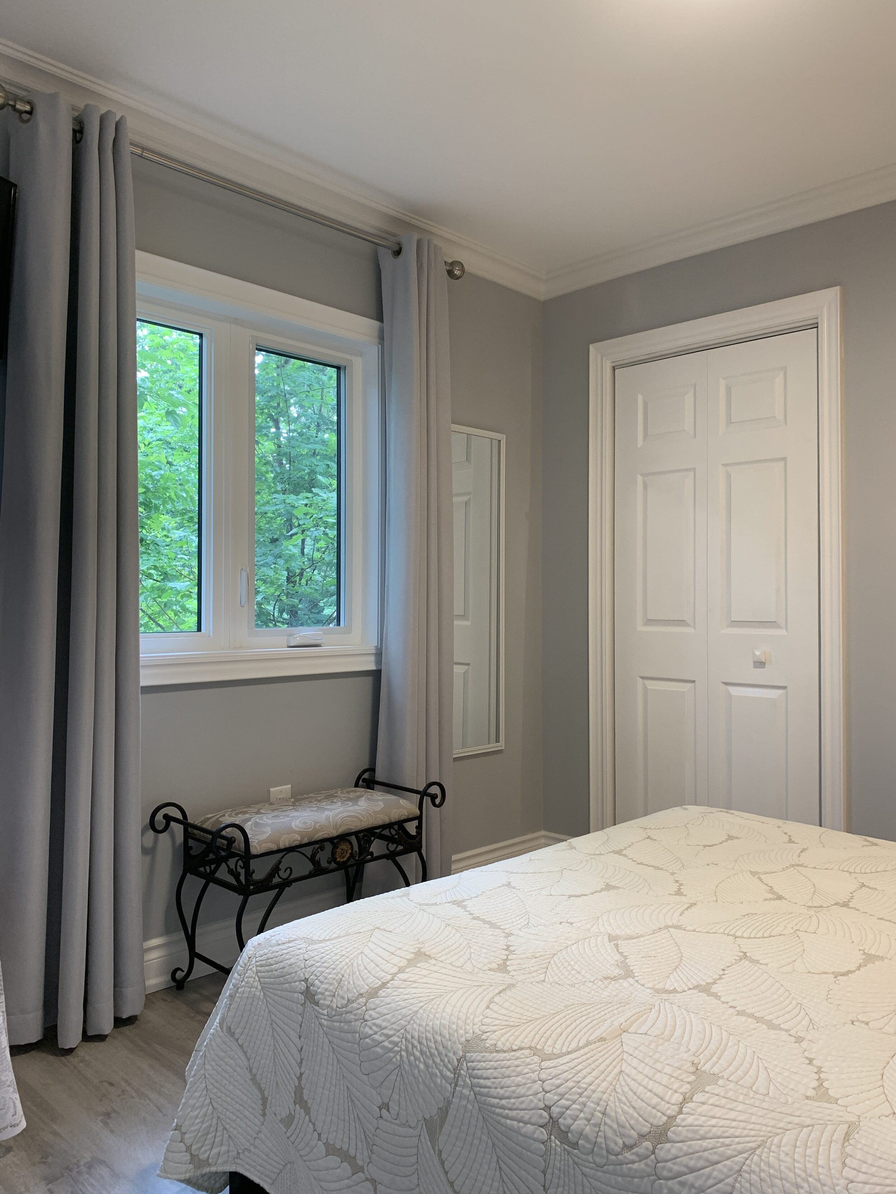 A bedroom with a bed, a window with curtains, a door, and a bench by the window.