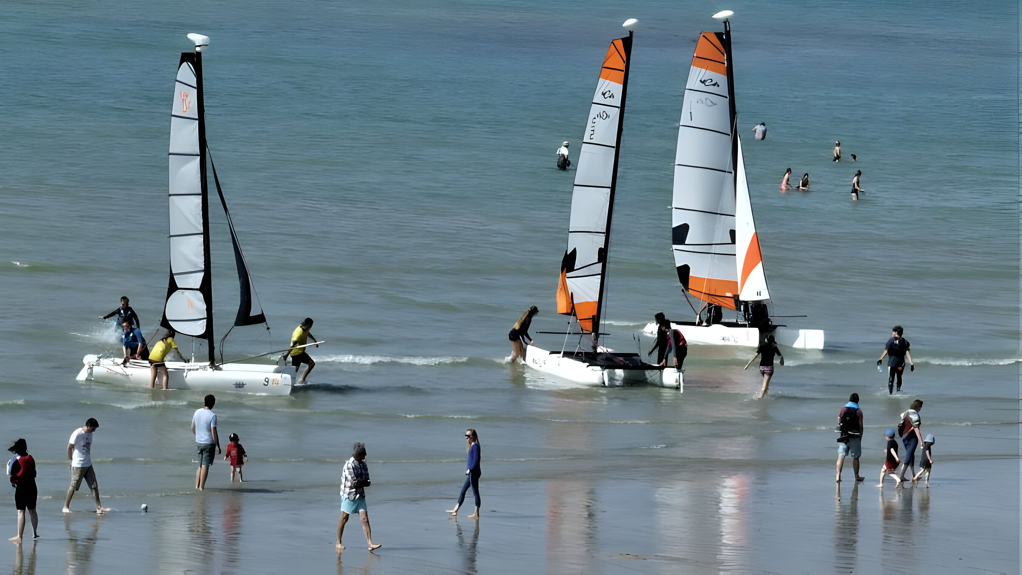 A beach with sailboats and people walking along the shore.