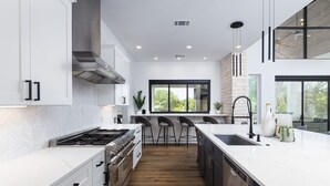 A modern kitchen with white cabinetry, a large island, and a view of the outdoors. - Lakefront 5BR w/ Pool, Hot Tub & Game Room. Sleeps 24. Family-Friendly (Seguin)