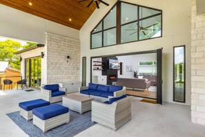 Un espace de vie extérieur moderne, doté de meubles en osier, d’une cheminée et d’une grande fenêtre donnant sur un jardin.