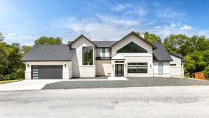 A modern two-story house with a garage, large windows, and a sloped roof. - Lakefront 5BR w/ Pool, Hot Tub & Game Room. Sleeps 24. Family-Friendly (Seguin)