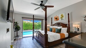 Ein geräumiges Schlafzimmer mit einem großen Bett, einem Deckenventilator, einem Fernseher und Blick auf einen Swimmingpool.