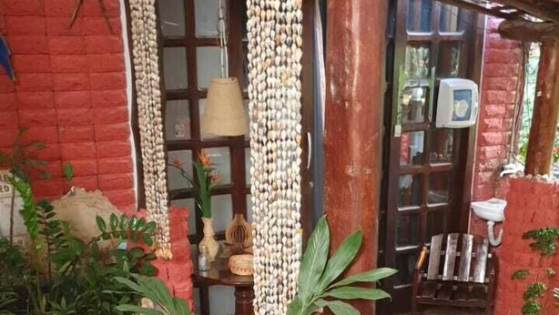 Una habitación con pared de ladrillo rojo, un banco de madera, una mesa con una planta y un adorno colgante.