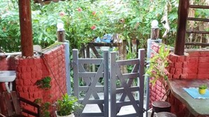 Un espacio al aire libre cubierto con suelo de piedra, mesas y sillas de madera, y una pared de ladrillo rojo.