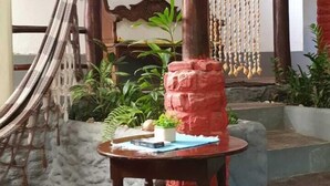 Un espacio de descanso rústico al aire libre con una mesa y taburetes, rodeado de plantas y un muro decorativo.