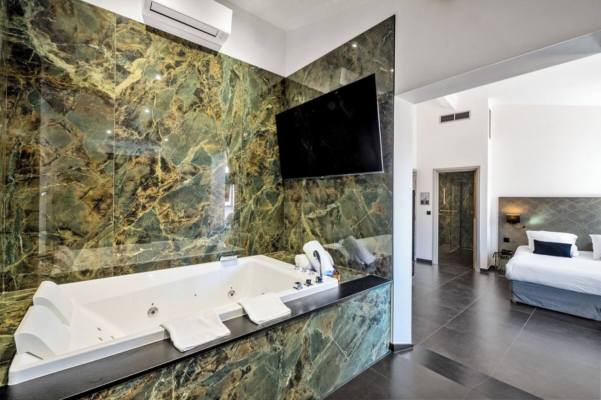 A modern bathroom with a large marble sink, a freestanding bathtub, and a flat-screen TV mounted above the mirror.