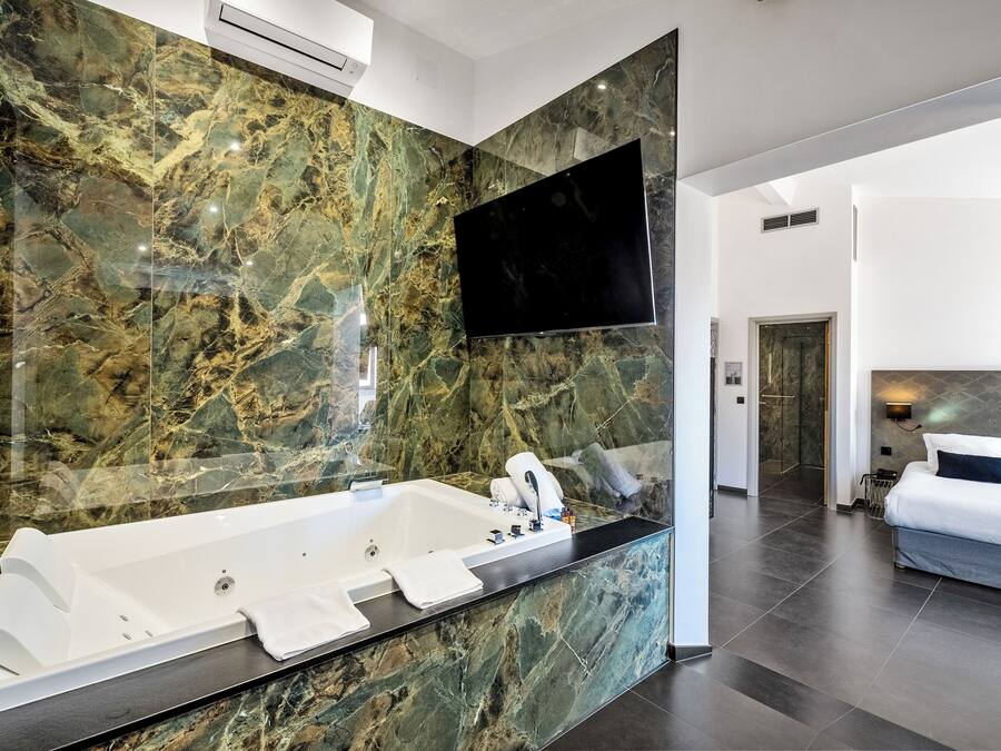 A modern bathroom with a large marble sink, a freestanding bathtub, and a flat-screen TV mounted above the mirror.