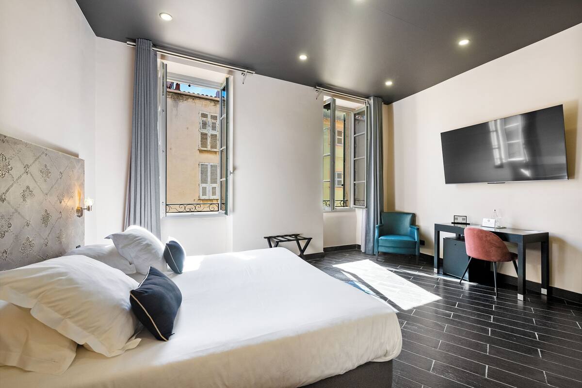 A modern hotel room with a large bed, a desk, a chair, and a TV on the wall.