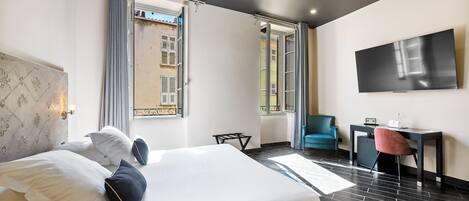 A modern hotel room with a large bed, a desk, a chair, and a TV on the wall.