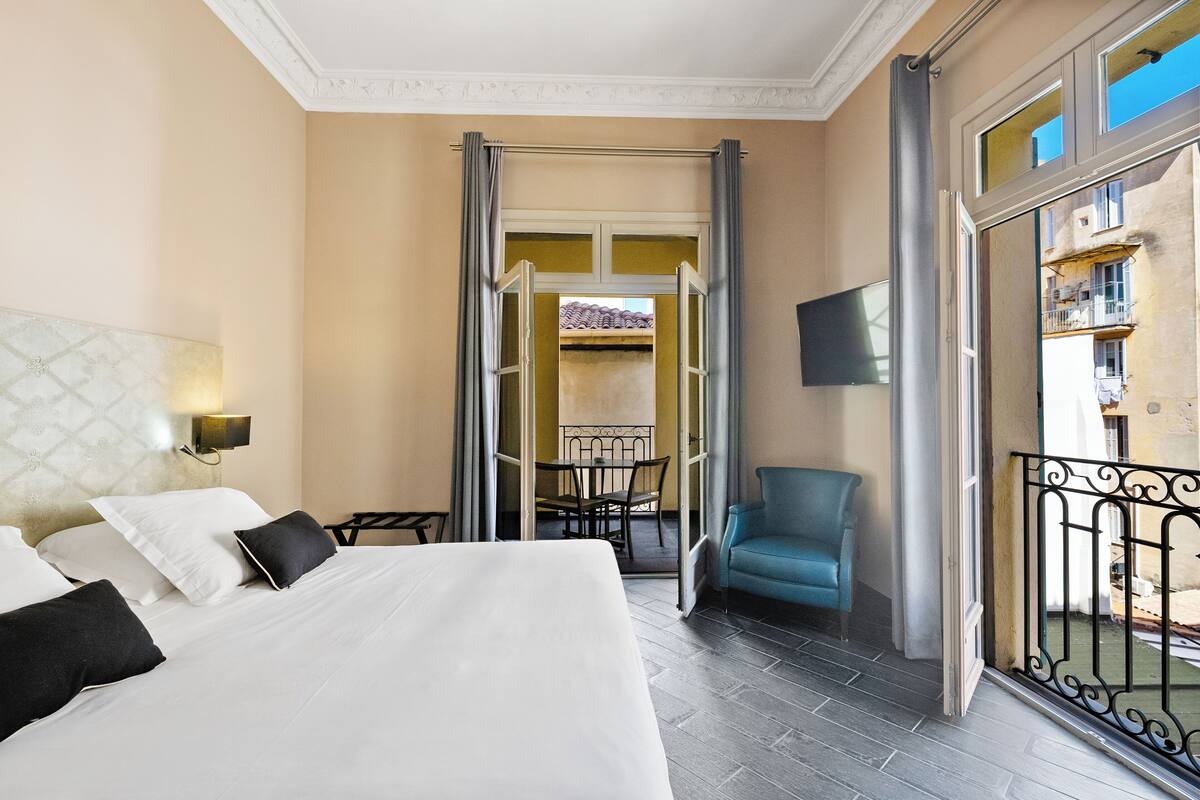 A hotel room with a bed, a chair, a TV, and a balcony with a view.