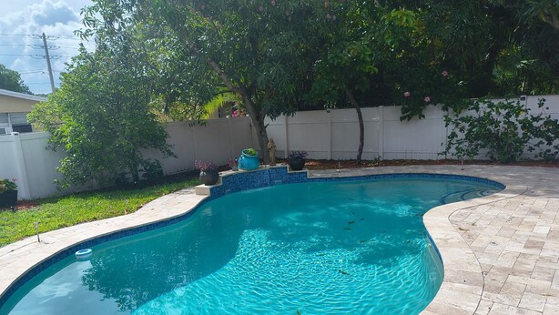 Ein Schwimmbecken mit geschwungener Kante, umgeben von einer gefliesten Terrasse und einem weißen Zaun.