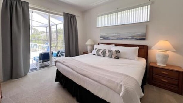 Een slaapkamer met een groot bed, een nachtkastje, een lamp, een raam met zonwering en uitzicht op de omgeving.