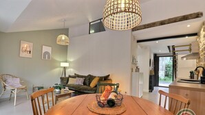 A modern living room with a wooden dining table, green sofa, and a kitchen area visible through an open door. - Victor - RIVES DU COUESNON (RIVES-DU-COUESNON)