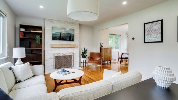 A modern living room with a white sofa, a round coffee table, a fireplace, and a dining area with a wooden table and chairs. - Cozy Modern Single Family 5BD 2BA Home (Falls Church)